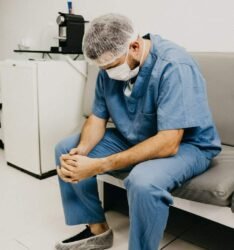 man wearing blue scrub suit and mask sitting on bench