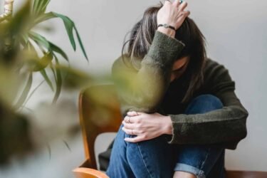 unrecognizable upset lady embracing knees sitting on chair